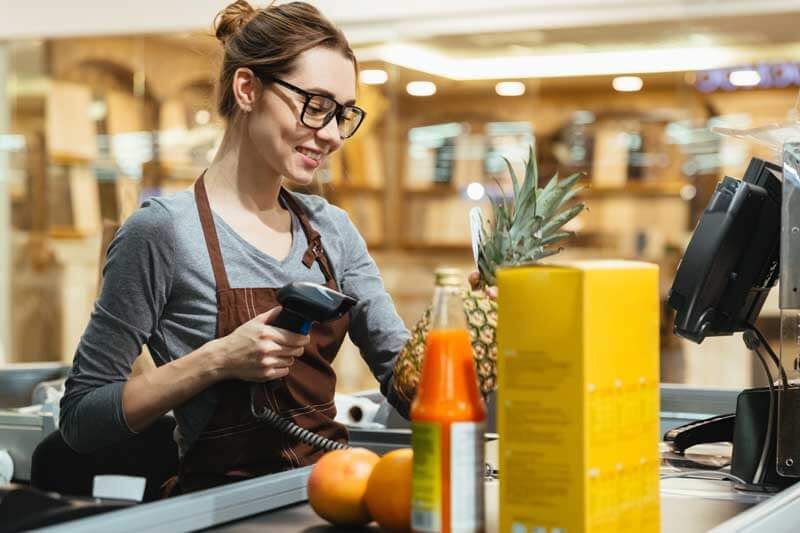 mulher usando um coletor de dados e uma impressora térmica para passar compras na esteira do caixa=